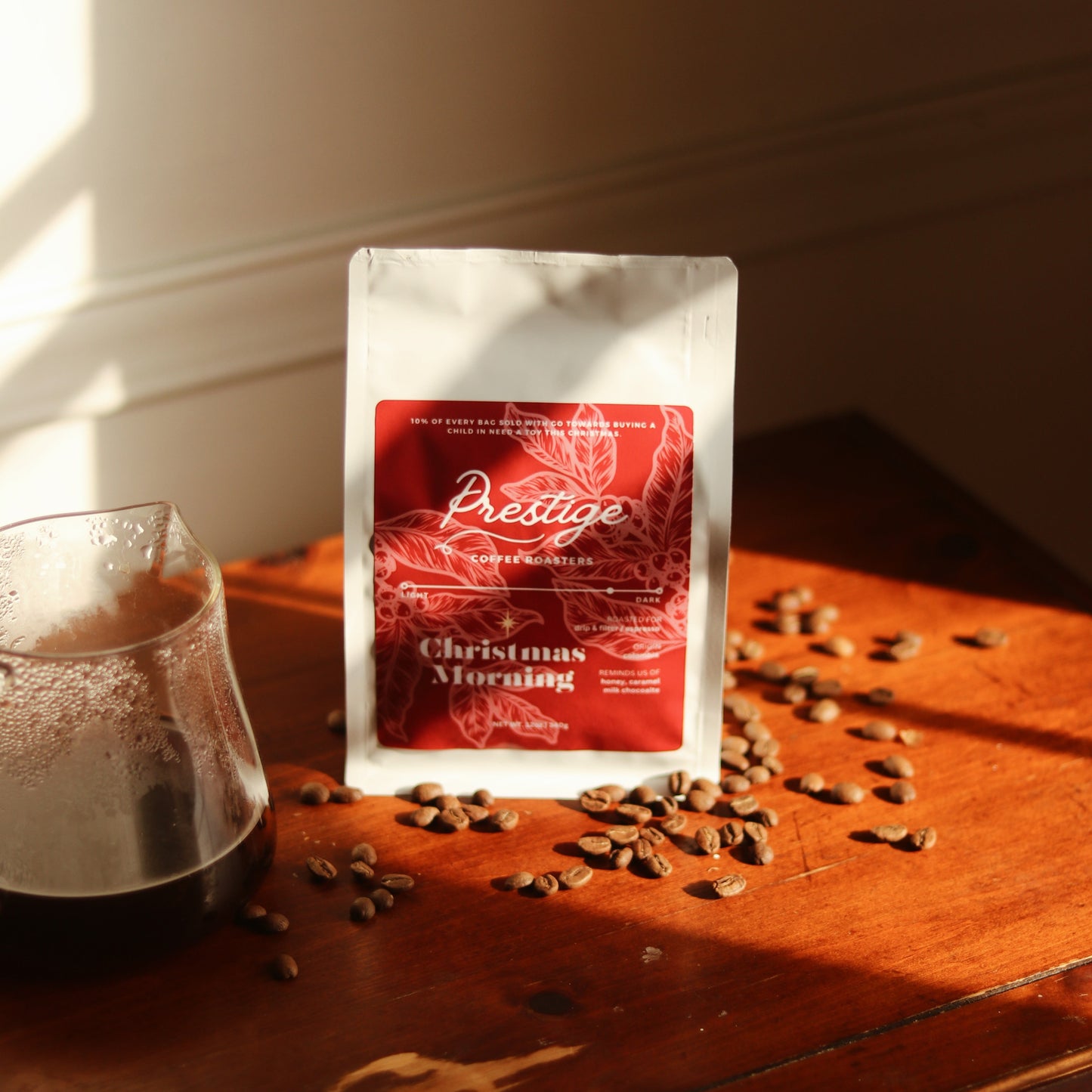 Coffee bag labeled 'Prestige' on a wooden surface with coffee beans and a glass of coffee.